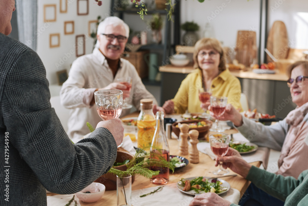 Man holding glass of red wine and saying the toast while other people listening to him at the table Man holding glass of red wine and saying the toast while other people listening to him at the table