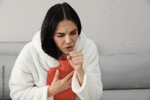 Ill woman with hot water bottle coughing at home