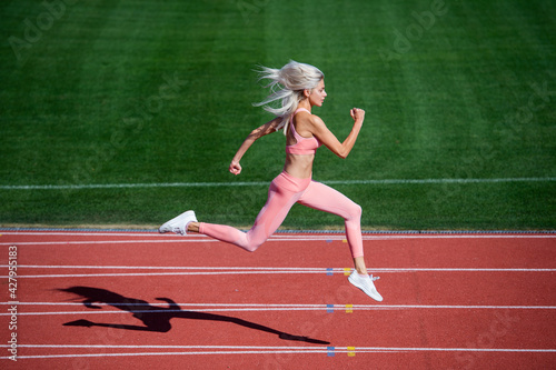 fit lady in fitness wear running on stadium racetrack while sport workout, energy