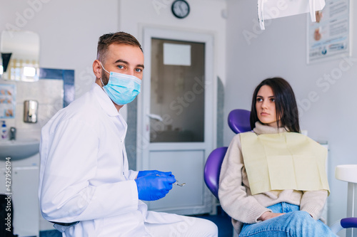 dentist in uniform holds dental tools and looks into the camera.