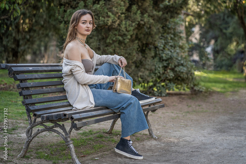 Pretty fashionable young woman sitting on a park bench