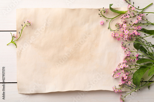 Beautiful Forget-me-not flowers and parchment on white wooden table, flat lay. Space for text