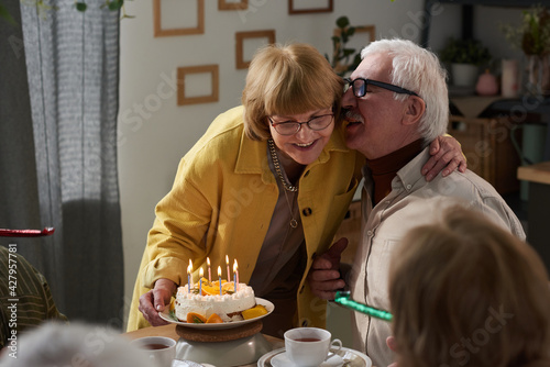 Happy senior couple embracing at the table while celebrating their anniversary with cake at home