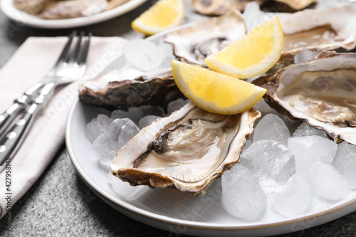 Fresh oysters with lemon and ice on grey table, closeup