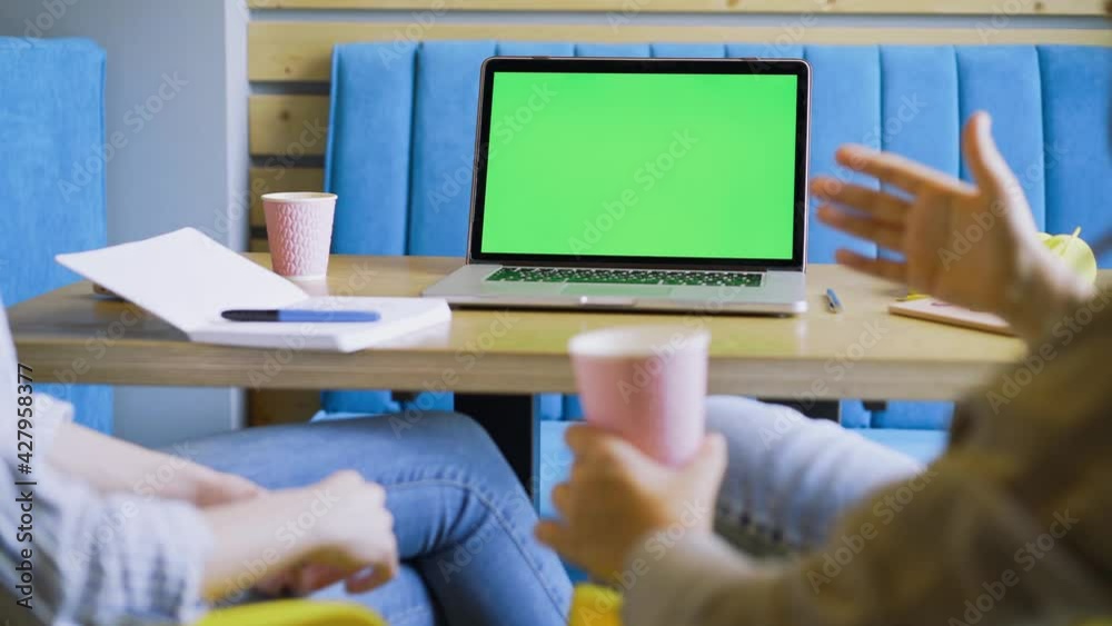 Female employees discuss new project sitting at table with contemporary laptop with green chromakey screen in light coworking office close backside view Female employees discuss new project sitting at table with contemporary laptop with green chromakey screen in light coworking office close backside view