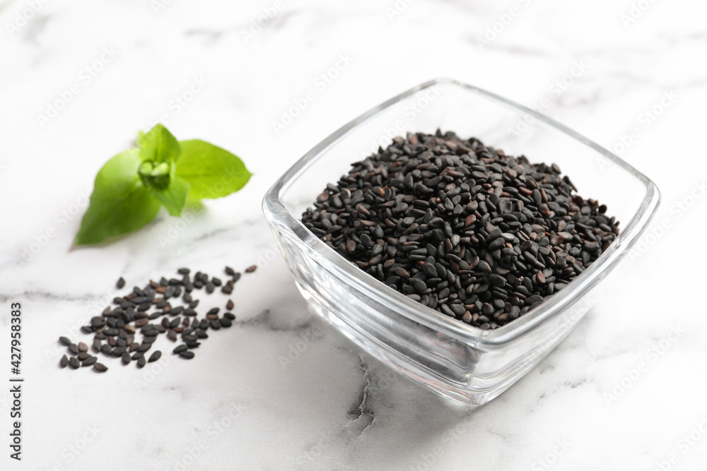 Black sesame seeds and green leaf on white marble table, closeup Black sesame seeds and green leaf on white marble table, closeup