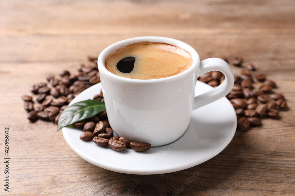 Cup of hot aromatic coffee and roasted beans on wooden table Cup of hot aromatic coffee and roasted beans on wooden table