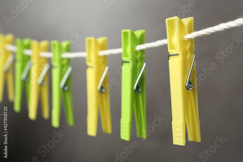 Colorful plastic clothespins on rope against grey background, closeup