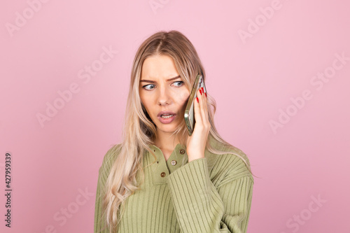 Pretty european woman in casual knitted sweater on pink background isolated hold phone having conversation with curious confused serious face