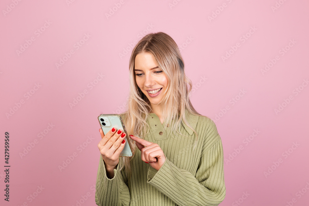 Pretty european woman in casual knitted sweater on pink background isolated happy look at phone with amazed surprised face Pretty european woman in casual knitted sweater on pink background isolated happy look at phone with amazed surprised face