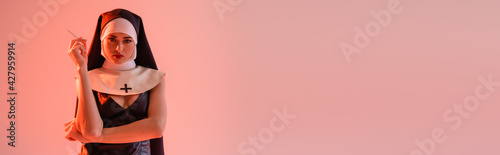 young nun in sexy dress holding cigarette isolated on pink, banner