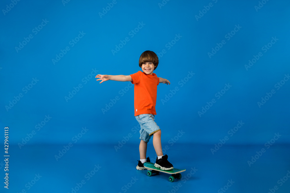 happy little boy stands with a skateboard on a blue background with space for text
