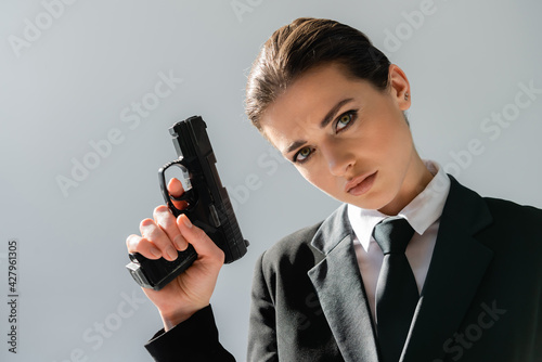 sensual, brunette woman looking at camera while holding handgun isolated on grey