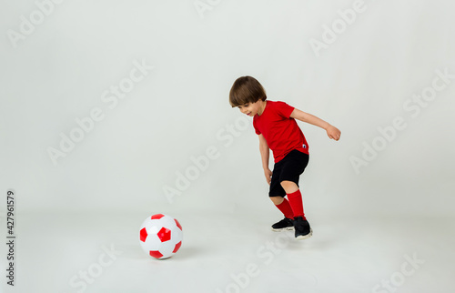 small boy in uniform plays with a soccer ball on a white background with space for text