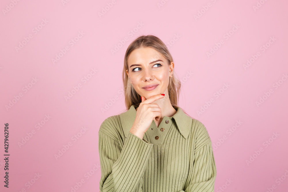 Pretty european woman in casual sweater on pink background looks to the side thoughtfully with a sweet smile Pretty european woman in casual sweater on pink background looks to the side thoughtfully with a sweet smile