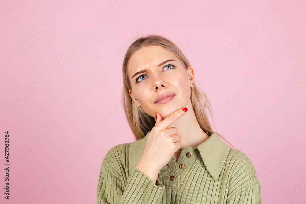 Pretty european woman in casual sweater on pink background looks to the side thoughtfully with a sweet smile Pretty european woman in casual sweater on pink background looks to the side thoughtfully with a sweet smile