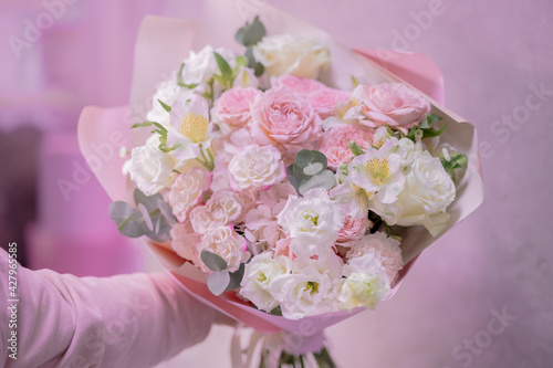 A hand holds a lush bouquet of light pink, white cute delicate small roses of different sizes, flowers of green leaves. Paper packaging. Romance. © SymbiosisArtmedia
