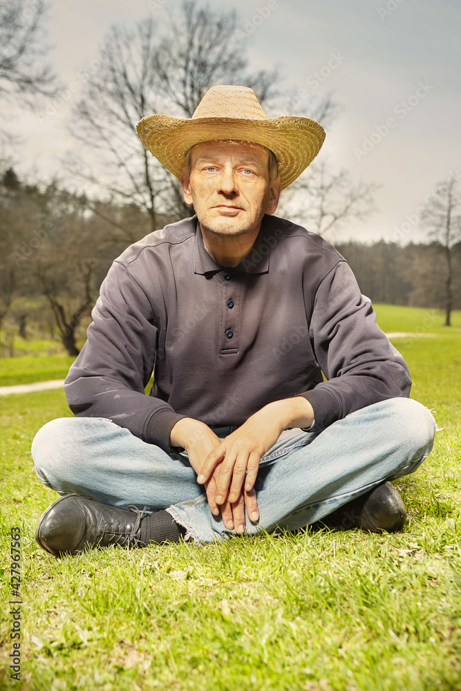 Natural older man in dark shirt and straw hat relaxing in sunny park