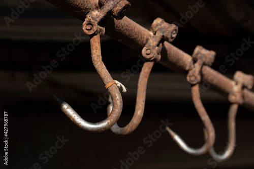 Tableau sur toile Rusty meat hooks hang from the ceiling against a dark background