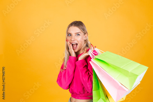 Pretty european woman in pink blouse on yellow background holding shopping bags shocked amazed excited isolated copy space