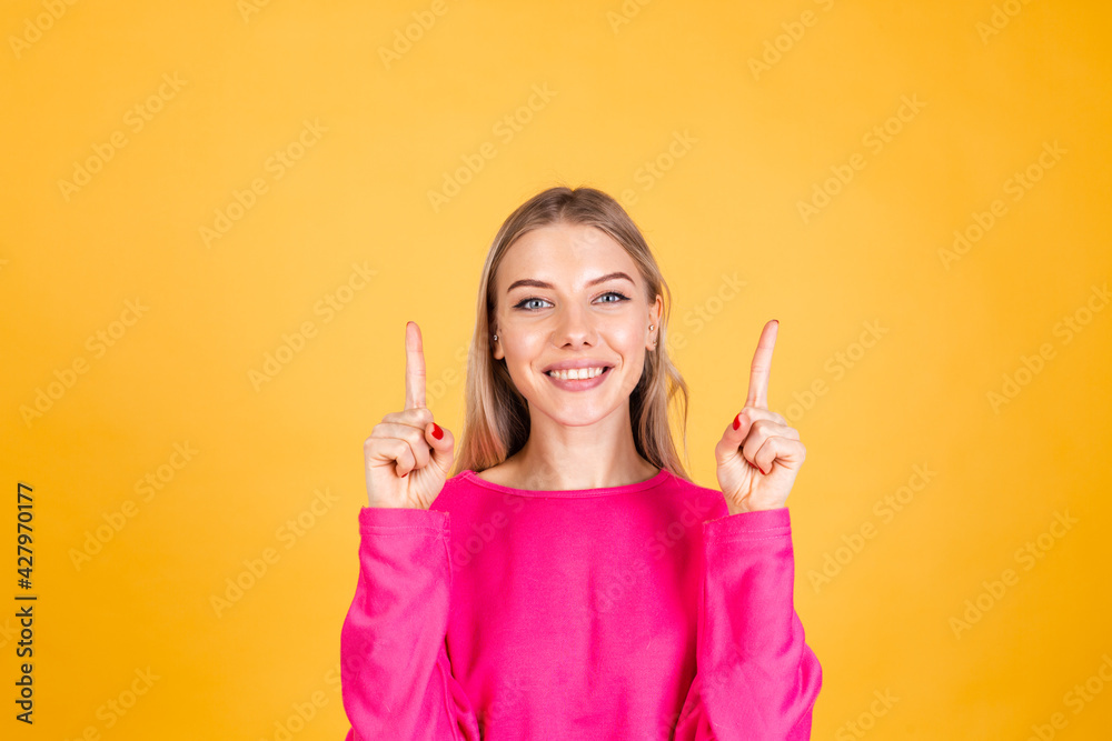 Pretty european woman in pink blouse on yellow background happy excited cheerful point up with index finger Pretty european woman in pink blouse on yellow background happy excited cheerful point up with index finger