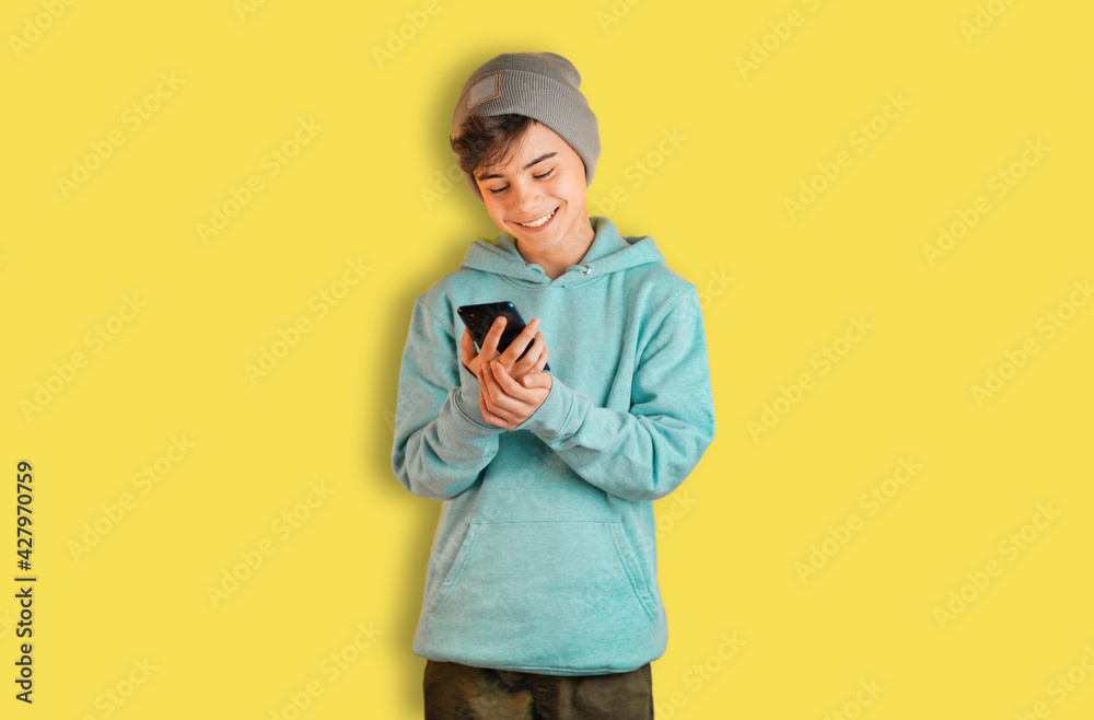 Portrait of positive cheerful boy using smartphone. teenager in stylish fashionable sweatshirt isolated on yellow background. shares news on social networks. internet provider and data security banner Portrait of positive cheerful boy using smartphone. teenager in stylish fashionable sweatshirt isolated on yellow background. shares news on social networks. internet provider and data security banner