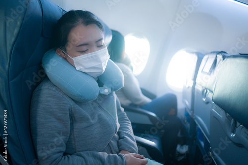 tourism and flying in times of covid19 - young sweet and tired Asian Chinese woman in face mask sitting on airplane cabin sleeping peacefully during flight photo