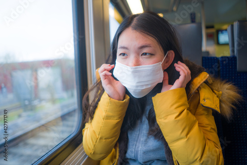 lifestyle portrait of young beautiful and thoughtful Asian Japanese woman in face mask as protection vs covid19 looking through window during train trip