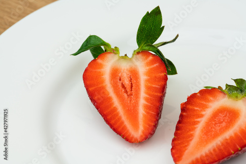 Red ripe strawberry slice on white plate on the table close up