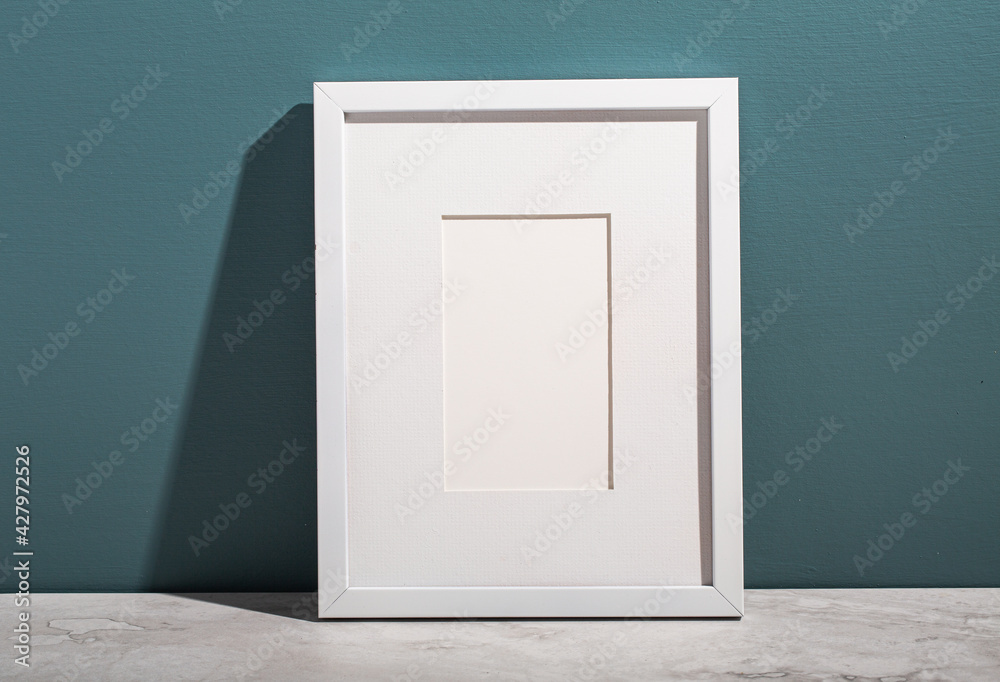 A white picture frame leans on an aegean teal painted wall. A white picture frame leans on an aegean teal painted wall.