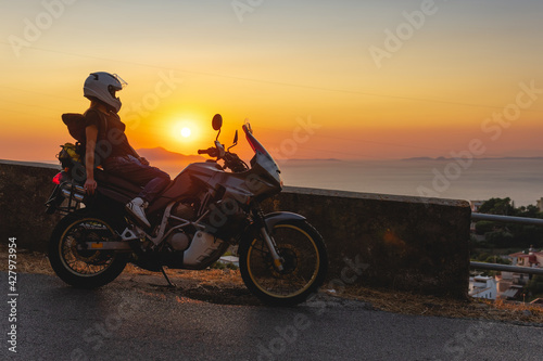 Biker girl sits on a adventure motorcycle. Freedom lifestyle concept. Romantic sunset. Sea and mountains, Copy space. Capri island. Sorrento Italy
