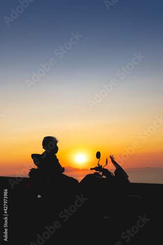 Woman biker silhouette over sunset, female riding motorcycle, motorbike driver traveling, lady look on the beach, freedom lifestyle. travel and vacation. Vertical photo