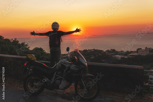 Motorcyclist man enjoy beautiful sunset arms spread out to the sides, sea and mountains. Destination. Motorcycle tour journey. copyspace for your individual text.