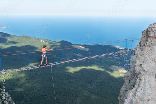 Young girl cross long aerial rope bridge on peak of Ai-Petri mountain in Crimea. Girl is brave and courage during adventure in mountains, Active lifestyle.