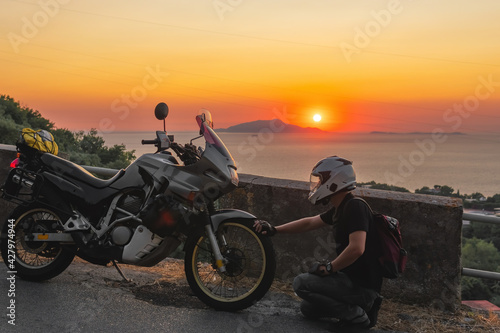 Motorcyclist man loves his bike, sunset, sea and mountains. Tourism and adventure. Motorcycle tour journey. copyspace for your individual text. © Sergey