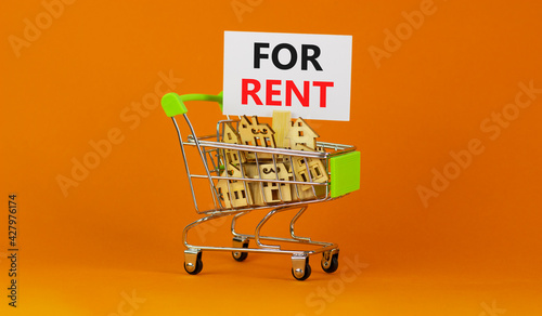 Real estate for rent symbol. Miniature shopping cart with wooden houses, words for rent. Beautiful orange background, copy space. Business and real estate for rent concept.