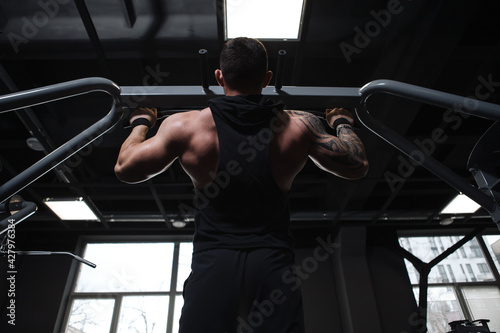 Low angle shot of a muscular male bodybuilder doing pull ups at the gym