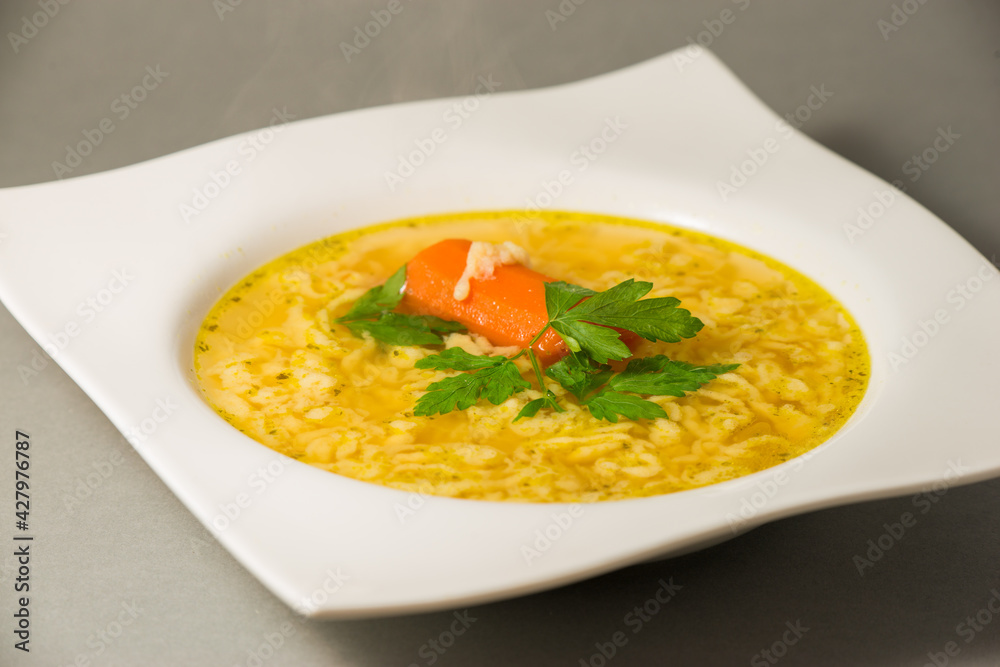 Chicken soup with egg noodles and red carrot, parsley top in white square plate