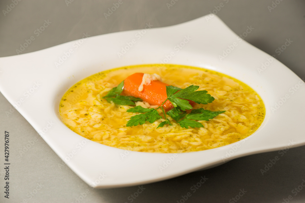 Chicken soup with egg noodles and red carrot, parsley top in white square plate Chicken soup with egg noodles and red carrot, parsley top in white square plate