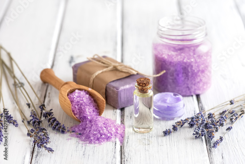 Lavender spa products on an old white wooden table. Body care products with lavender-oil, salt, cream, soap and dried lavender flowers. Selective focus.