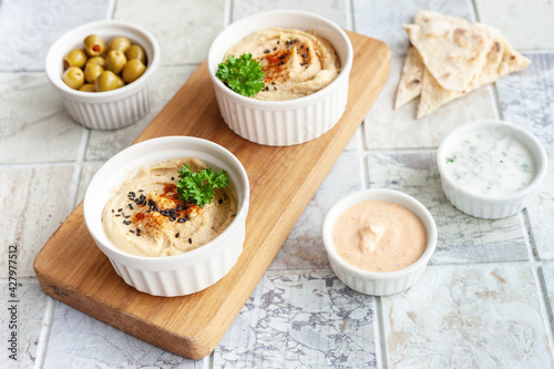 Bowl of hummus, traditional Jewish, Arabian, Middle Eastern food from chick-peas with dips and with pita flatbread on ceramic tile background. Close up, selective focus