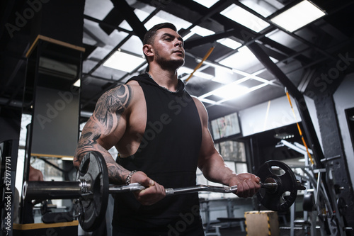 Low angle shot of a tattooed bodybuilder with ripped body exercising with barbell