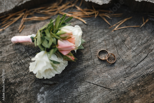 Wedding rings and boutonniere on a wood texture background.
