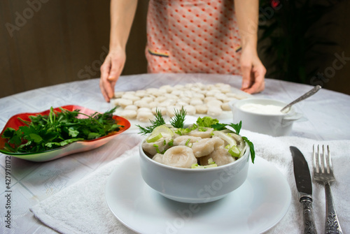 Bowl of cooked homemade dumplings, garnished with green dill and parsley leaves on the background of female hands.Selective focus.