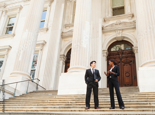 A well dressed man and woman converse on the steps of a legal or municipal building. Could be business or legal professionals or lawyer and client.