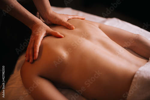Young unrecognizable woman gets professional back massage in spa salon. Beautiful naked girl with perfect skin gets relaxing massage. Concept of luxury professional massage. Concept of body care.