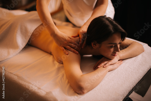 Brunette female with closed eyes is relaxing during back massage lying on massage table in spa salon. Concept of luxury professional massage. Concept of body care.