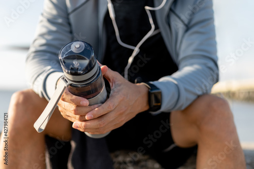 Man runner is holding bottle of water. Tired man is drinking water after run exercise.