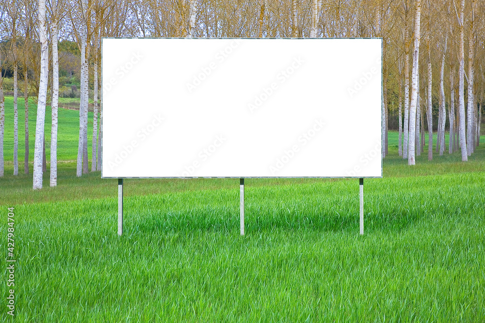 Blank advertising signboard in a green field with trees on background - concept with copy space and space for inserting text Blank advertising signboard in a green field with trees on background - concept with copy space and space for inserting text