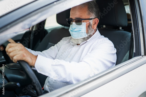 A senior man in a medical surgical mask driving a car. Coronavirus pandemic concept. © ManuPadilla